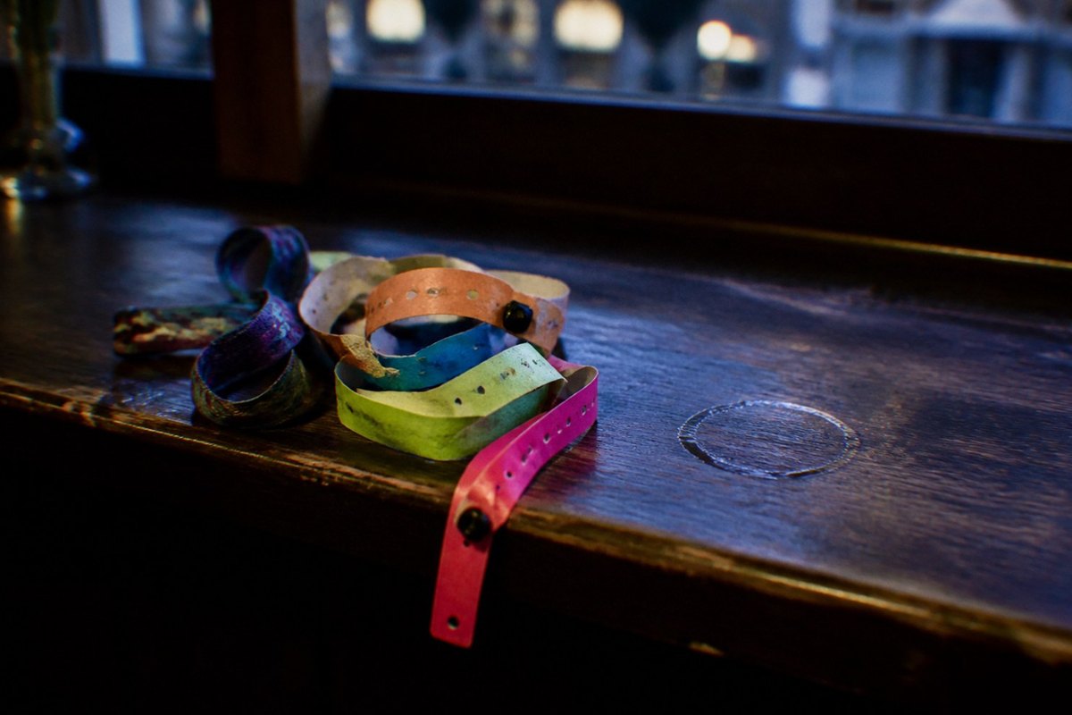 A worn pile of neon plastic and paper festival wristbands and a crumpled lanyard on a dark bar counter