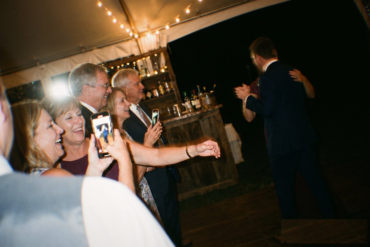 Guests standing at the edge of a dance floor photographing a first dance with their phones