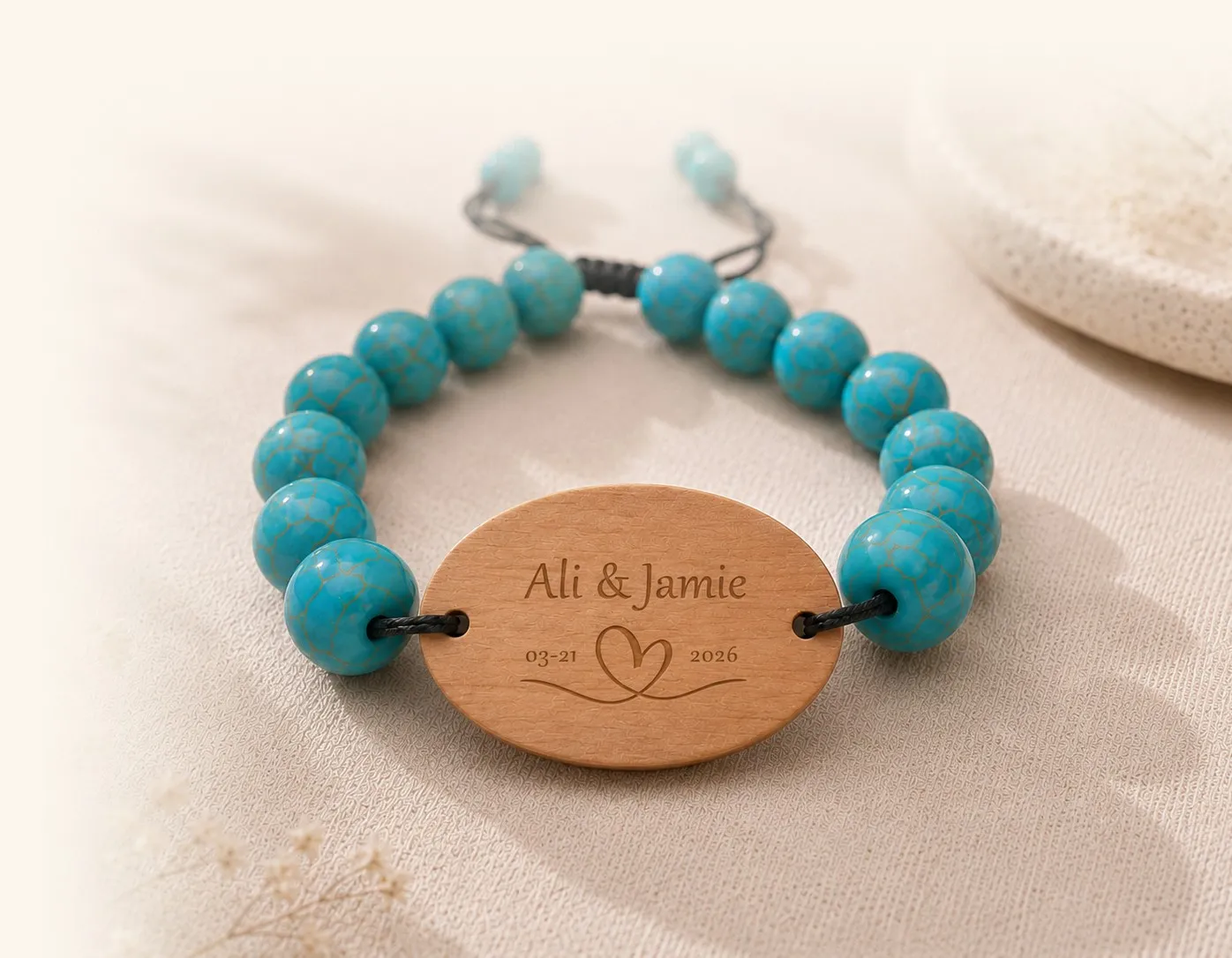 An engraved turquoise-and-wood WearableWedding bracelet — the tag reads “Ali & Jamie” — resting on linen.